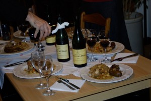 Four bottles on the table, and a whole bunch of glasses and food.